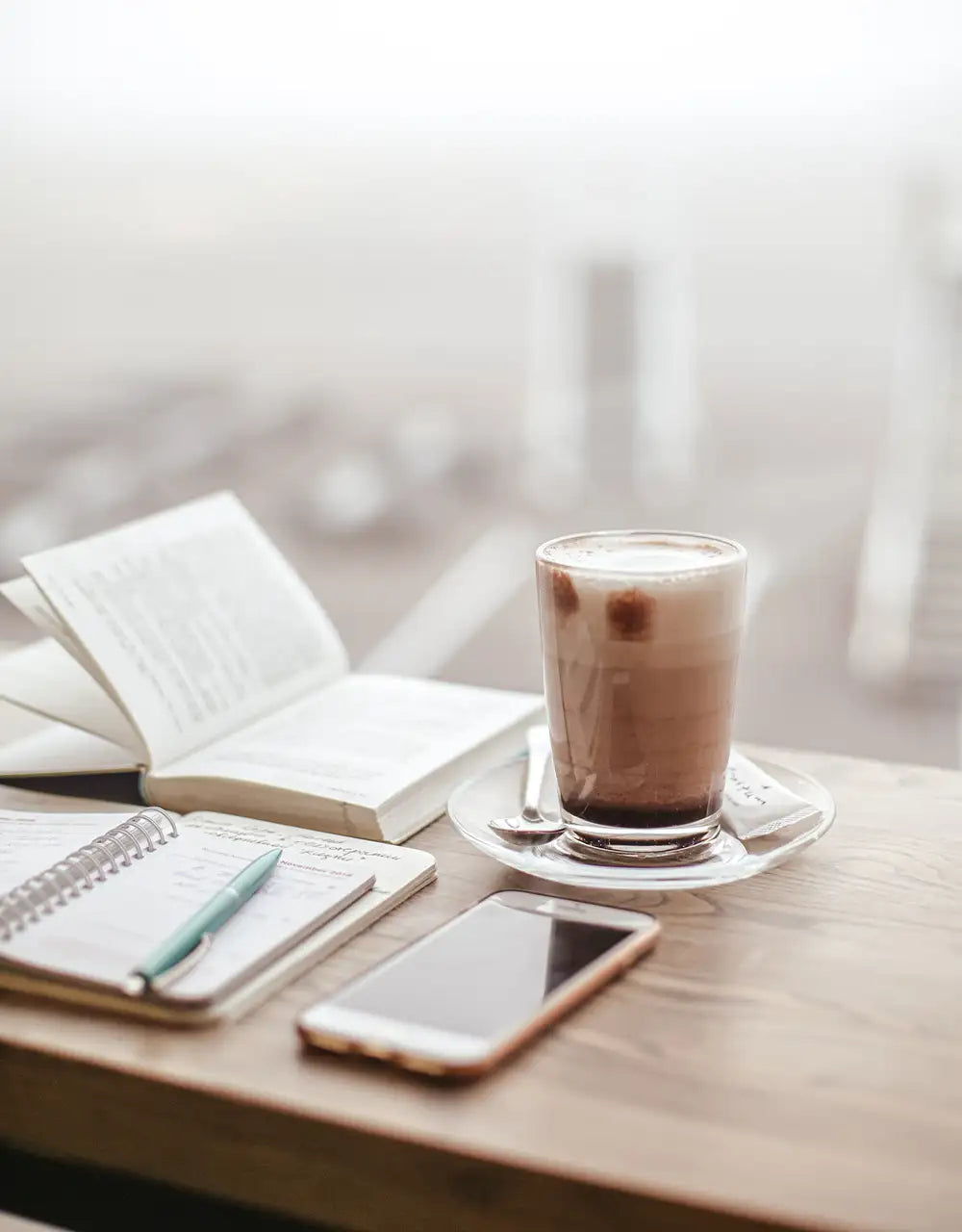en kaffe, iphone och en bok liggandes på bar