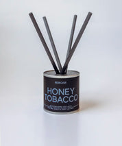 Honey Tobacco doftpinnar i metallburk med stilrena svarta fiberstickor ⎯ fotograferat mot ljus ren bakgrund.