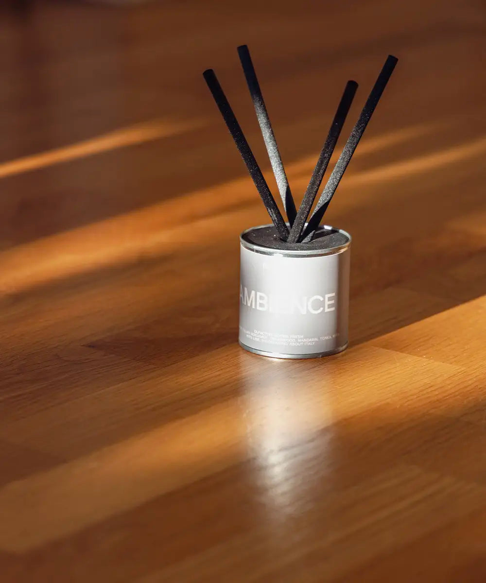 Ambience doftspridare med gråbeige etikett på ljust parkettgolv i minimalistisk miljö.