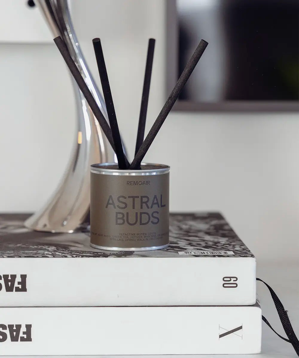 Astral Buds doftset i stilren silverbehållare placerad på inredningsböcker.