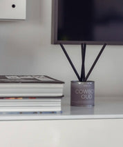 Stilren silverbehållare för Cowboy Oud doftpinnar placerad på en trave exklusiva böcker.