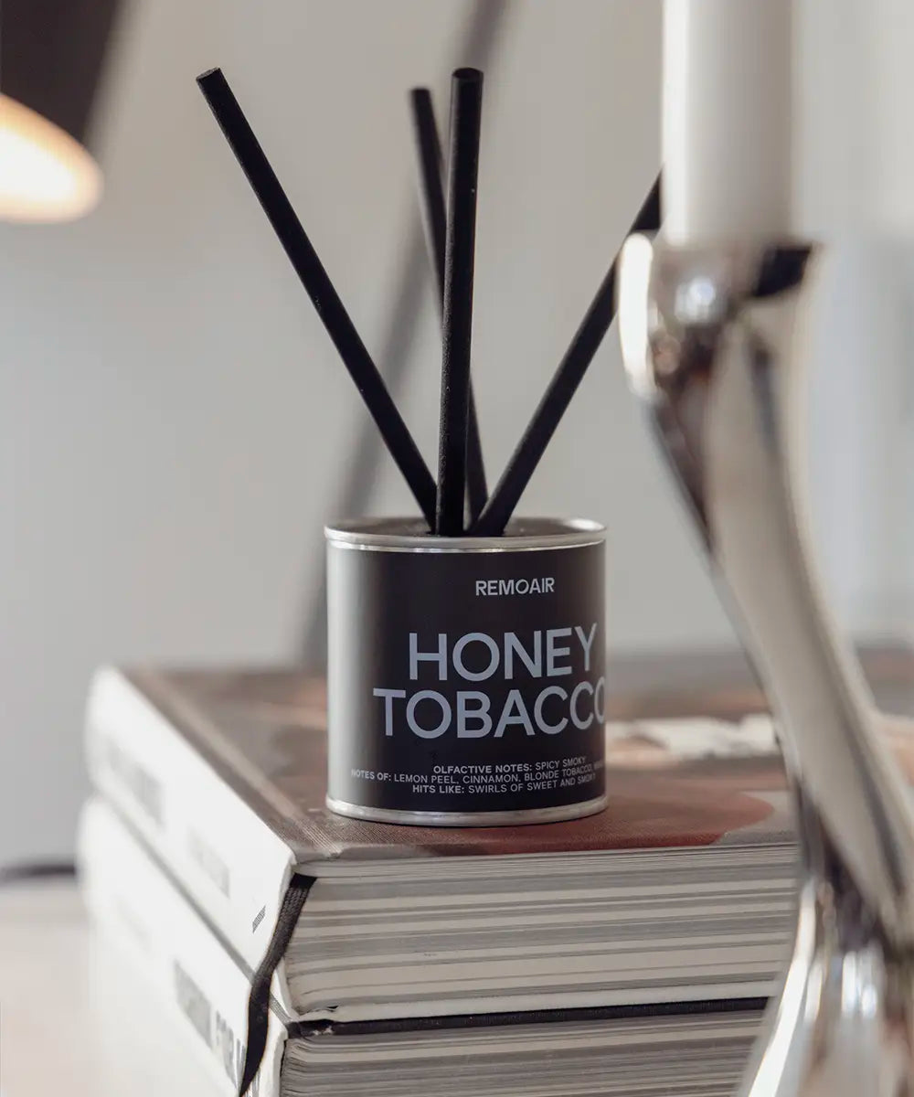 Honey Tobacco doftpinnar med mörkbrun etikett och svart lock på ett stilrent sidobord.
