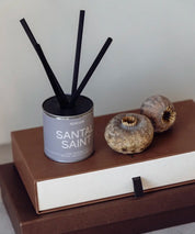 Lyxig doftspridare Santal Saint med gråbeige etikett och korta svarta stickor i stilren inredning.