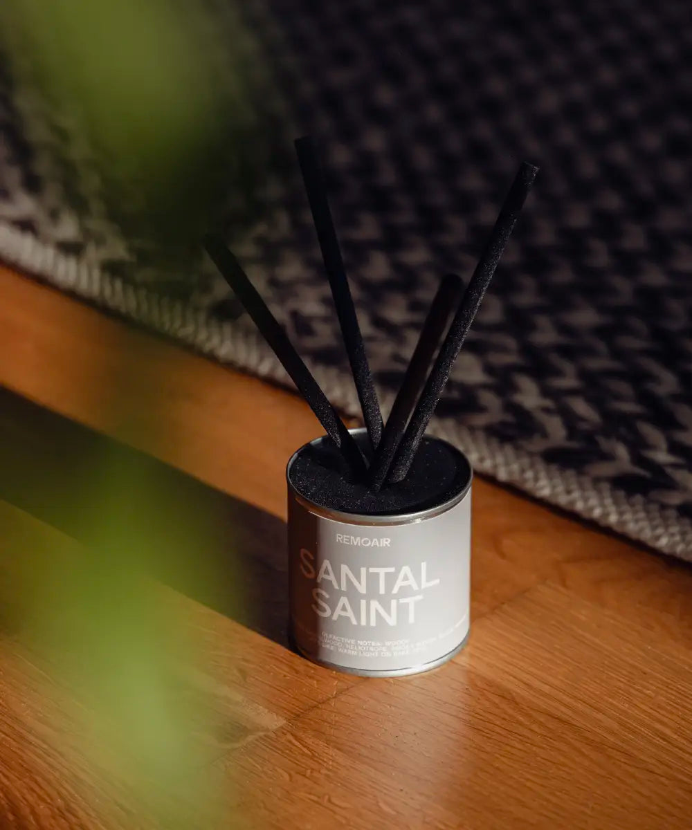 Santal Saint doftpinnar i silver plåtburk på ljust parkettgolv i varmt, naturligt solsken.