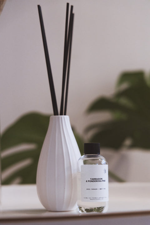 Refill till doftljus står framför en vit vas med pinnar i