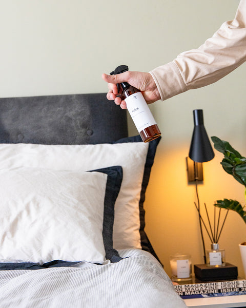En person sprayar doftspray över sängkläderna på en fint bäddad säng